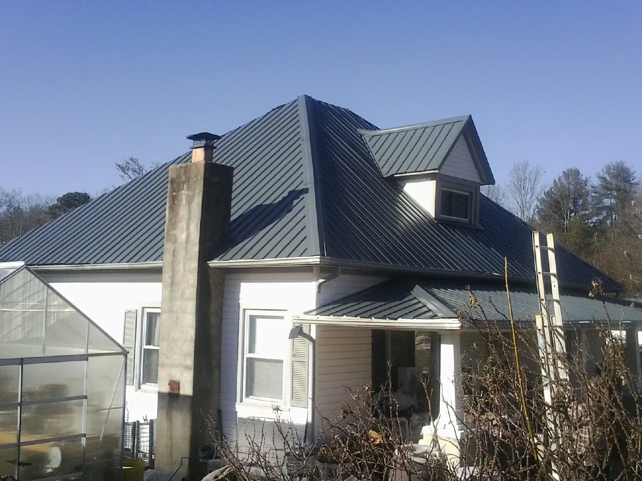 Dark blue standing seam metal roof on a white farmhouse with dormer — Slate & Tile Roof Repair by Roofing Brothers in Roan Mountain
