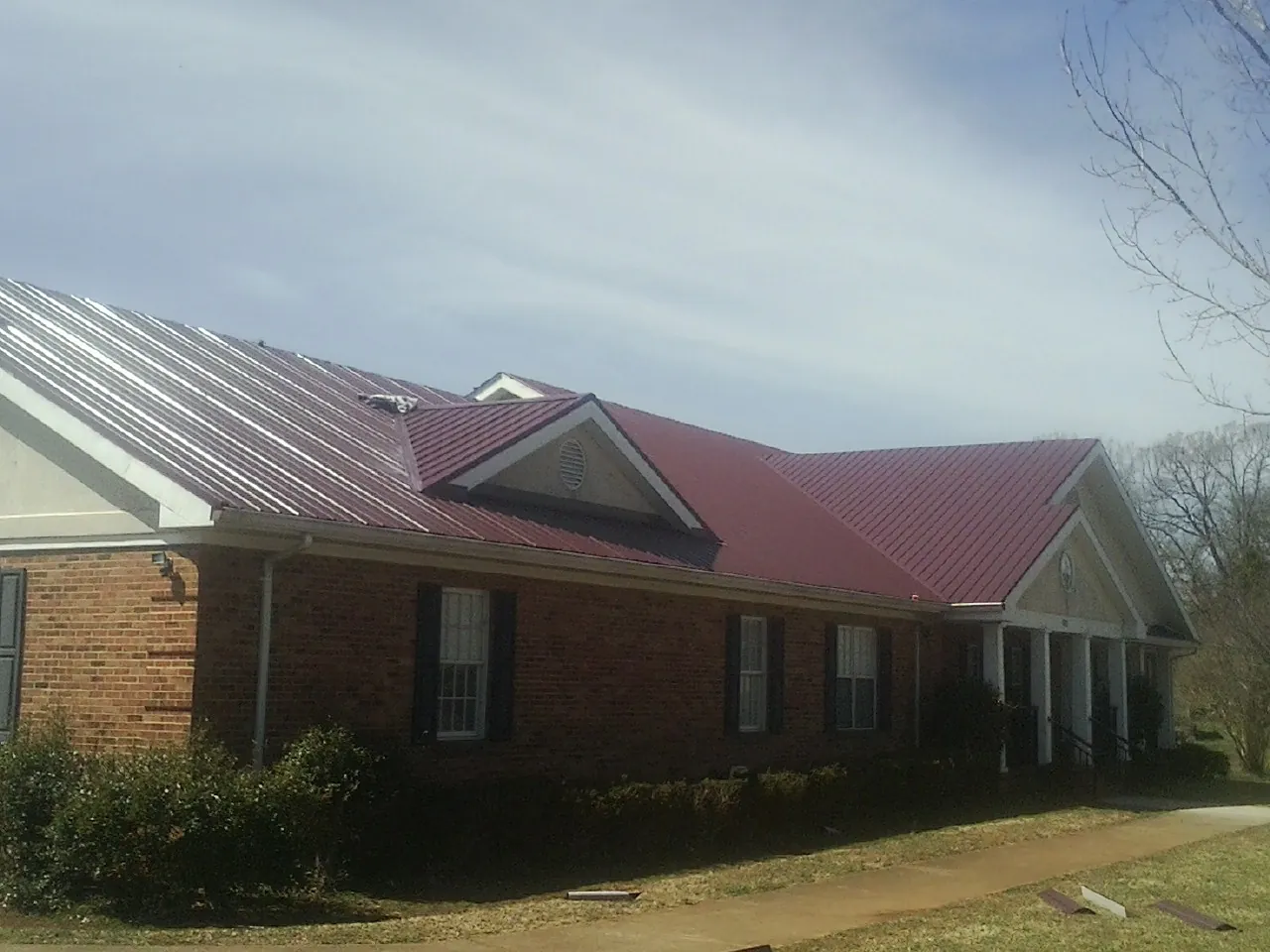 Red metal roof with gabled entries on a long brick building, from a Hail Damage Roof Repair job in Roan Mountain