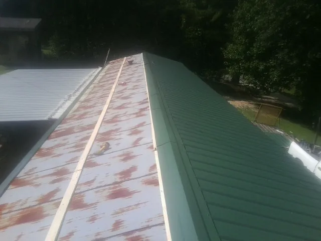 Old rusted panels beside newly installed green metal roofing — Wind Damage Roof Repair by Roofing Brothers in Roan Mountain