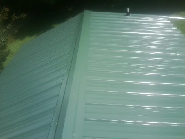 New green metal panels meeting at the ridge of a roof — Flat Roof Repair work by our crew in Roan Mountain