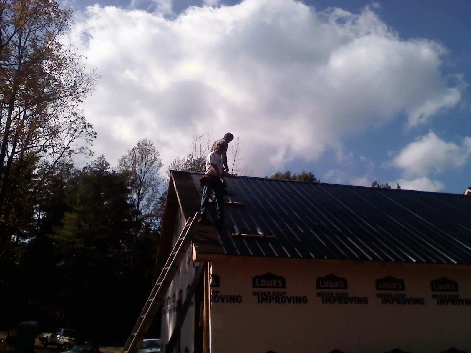Roofer fastening dark metal panels high against a cloudy sky, from a Roof Inspection job in Roan Mountain