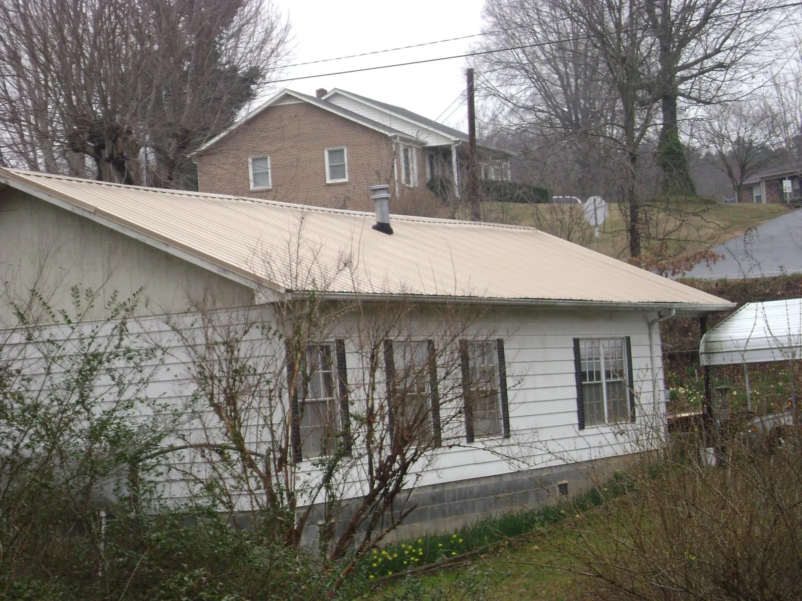 Tan metal roof on a white sided house set into a hillside — Commercial Roofing by Roofing Brothers in Roan Mountain