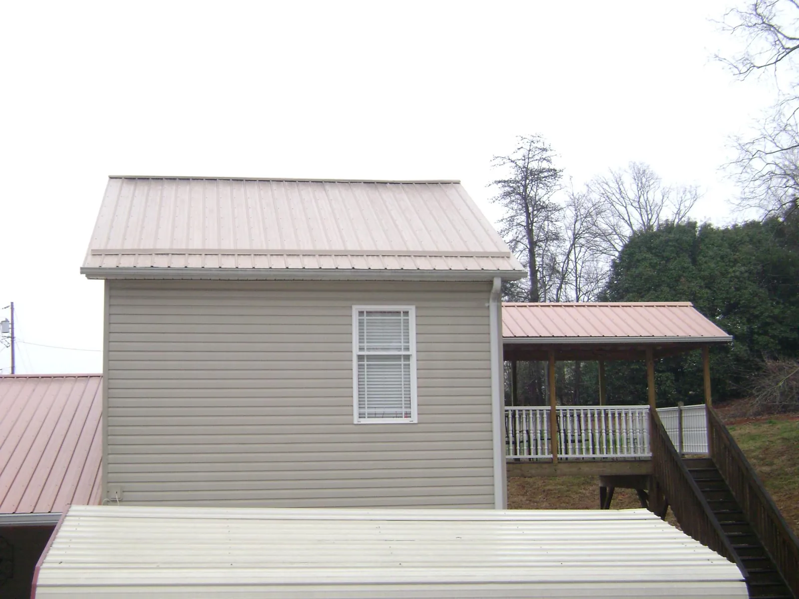 Tan metal roofs on a two story addition and attached porch, from a Roof Replacement job in Roan Mountain